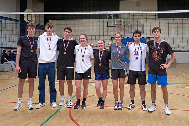 Mešana ekipa treh deklet in treh fantov stoji objeta na odbojkarskem igrišču. Okrog vratu imajo zlate medalje.