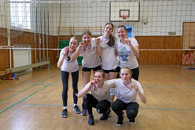 Šest deklet, igralk dbojke, nasmejane držijo v rokah zlate medalje. Tri so medaljo stisnile celo z zobmi, da bi pokazale, da je medalja prava.