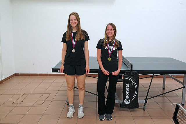 Slika prikazuje dekleti, ki sta tekmovali v namiznem tenisu. Okrog vratu nosita vsaka svojo medaljo.