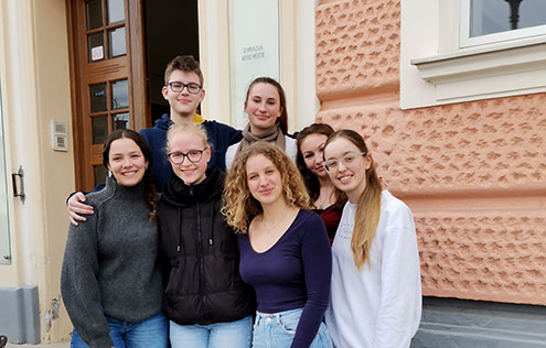 Šest dijakinj in dijak stojijo na stopnišču pred Gimnazijo Novo mesto, kjer je potekalo državno tekmovanje iz znanja psihologije. Zrejo v kamero, so nasmejani.