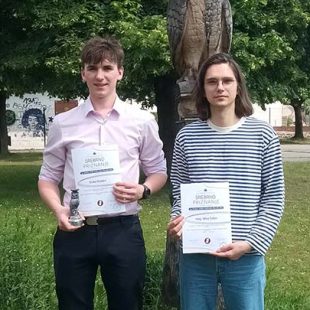 Na fotografija sta dijak in njegov učitelj kemije. V rokah držita plakati za srebrno priznanje, dijak poleg tega še srebrn kipec sovice, zaščitnega znaka tekmovanja mladih raziskovalcev.