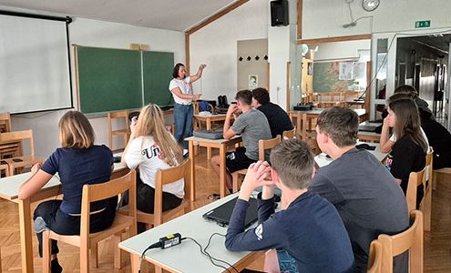 Dijaki so v učilnici, na mizah imajo prenosne računalnike. Poslušajo razlago učiteljice.