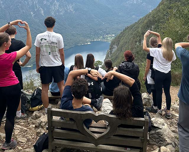 Dijaki stojijo na robu hriba in gledajo na Bohinjsko jezero v dolini.