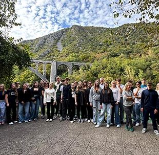 Velika skupina dijakov stoji na razgledni ploščadi, v ozadju je visok Solkanski most nad reko Sočo.