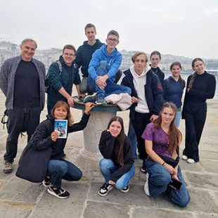 Devet dijakov, profesor in profesorica stojijo na kamnitem pomolu v Trstu.