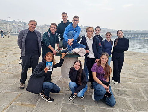 Devet dijakov, profesor in profesorica stojijo na kamnitem pomolu v Trstu.