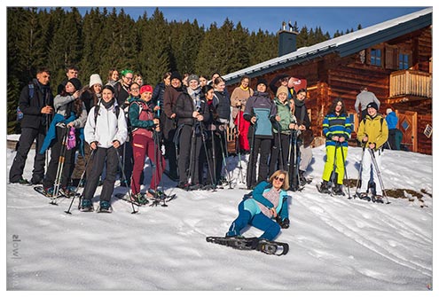 Večja skupina dijakov stoji na zasneženem pobočju, obsijanem s soncem. Na nogah imajo krplje, ki jim omogočajo lažjo hojo po snegu.