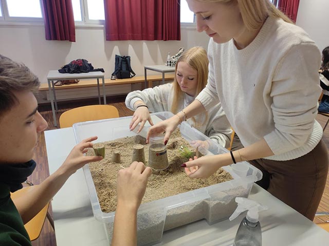 Dve dijakinji in dijak oblikujejo različna geometrijska telesa iz mivke.