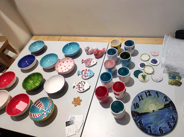 Fotografija prikazuje pisano pobarvane keramične izdelke: skodelice, lončke in magnetke.