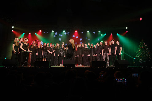 Na odru stoji številčen pevski zbor z dirigentko.