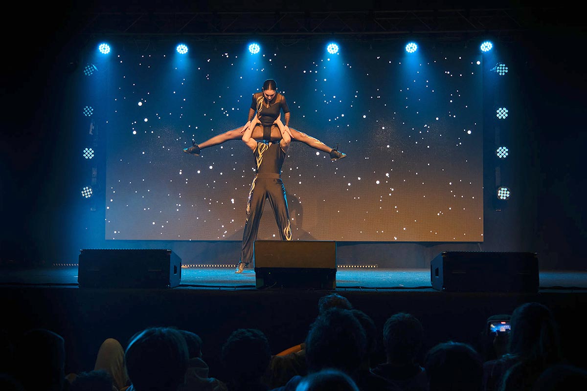 Prizor z nastopa: dijak in dijakinja plešeta akrobatski rokenrol. Plesalec je soplesalko dvignil visoko v zrak, ona je v zraku naredila špago.