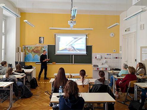 Potopisno predavanje o Afganistanu: Predavatelj živahno govori o fotografiji, ki je prikazana na projekcijskem platnu. Dijaki predavanje spremljajo iz šolskih klopi.