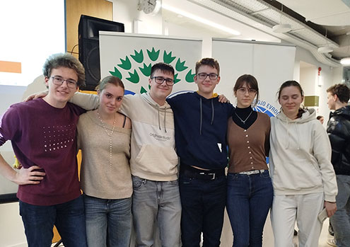 Tri dijakinje in trije dijaki stojijo pred panojem z znakom Ekošole. So nasmejani, objemajo se čez ramena.