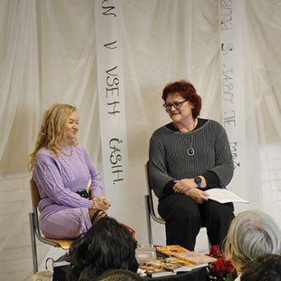 Pesnica Dragica Čarna in učiteljica slovenščine Tatjana Cvetko sedita pred občinstvom. Na nizki mizi pred njima so pesniške zbirke Dragice Čarna.