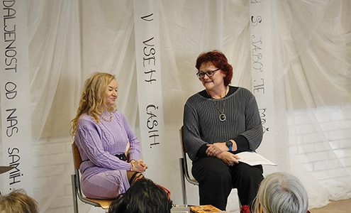 Pesnica Dragica Čarna in učiteljica slovenščine Tatjana Cvetko sedita pred občinstvom. Na nizki mizi pred njima so pesniške zbirke Dragice Čarna.