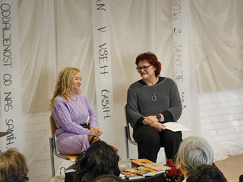 Pesnica Dragica Čarna in učiteljica slovenščine Tatjana Cvetko sedita pred občinstvom. Na nizki mizi pred njima so pesniške zbirke Dragice Čarna.