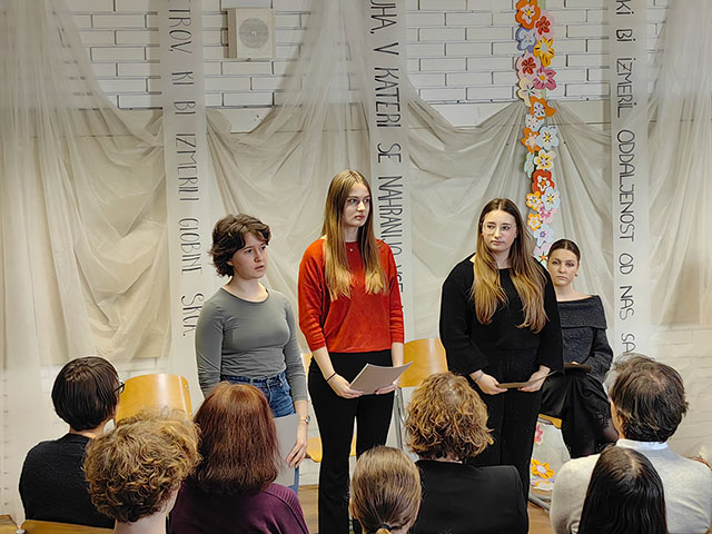 Tri dijakinje stojijo pred občinstvom. Ena od njih interpretira pesem Dragice Čarna.