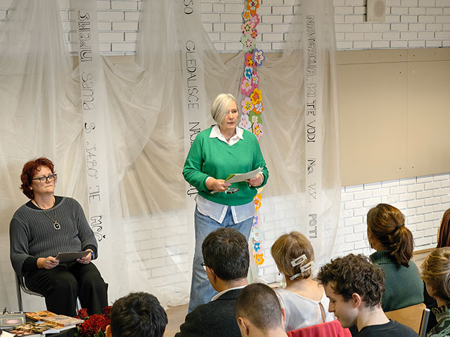 Govor predsednice Kulturnega društva Anice Černeje, Helene Osterman. Stoji pred občinstvom v učilnici. 