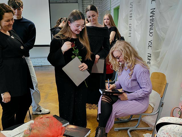 Fotografija je bila posneta po zaključku prireditve. Pesnica Dragica Čarna piše posvetilo v knjigo, ki jo je podarila dijakinji.