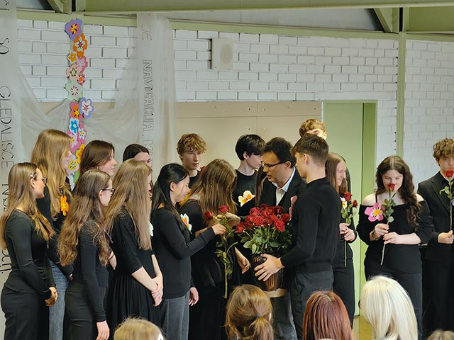 Fotografija je bila posneta po zaključku prireditve. Ravnatelj deli rdeče vrtnice pevcem v pevskem zboru.