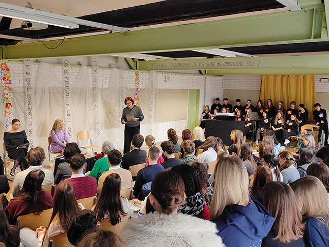 Govor učiteljice Tatjane Cvetko pred učilnico, polno dijakov. Na stolu poleg nje sedi gostja, pesnica Dragica Čarna.