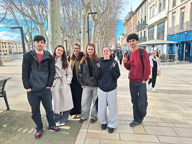 Šest dijakov je slikanih na ulicah mesta Narbonne. Za njimi so drevesa, ki imajo še gole veje.