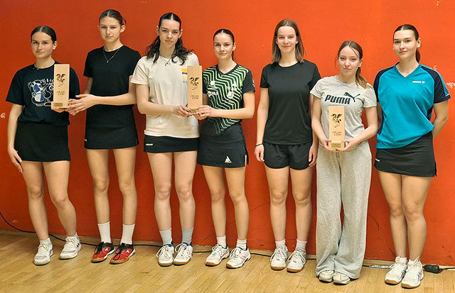 Sedem dijakinj stoji ena poleg druge. Nekatere imajo v rokah priznanje za doseženo mesto na tekmovanju v namiznem tenisu. Oblečene so v športne majice in kratke hlače.