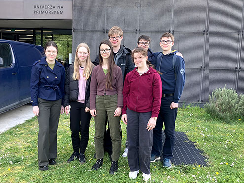 Sedem dijakov in dijakinj stoji na trati pred vhodom v Fakulteto za matematiko, naravoslovje in informacijske tehnologije.