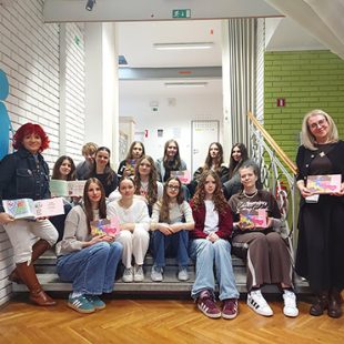 Dijaki sedijo na stopnicah hodnika in v rokah držijo odprte knjige, pri nastanku katerih so sodelovali.