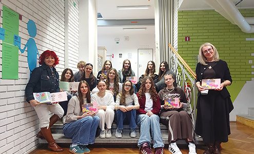 Dijaki sedijo na stopnicah hodnika in v rokah držijo odprte knjige, pri nastanku katerih so sodelovali.