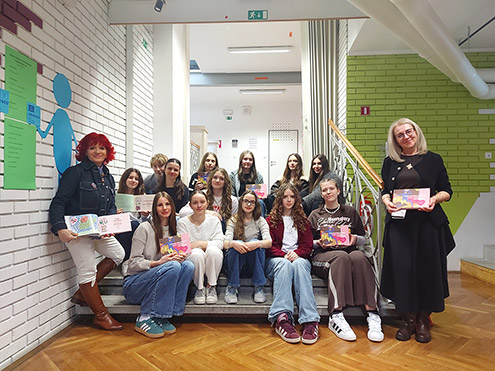 Dijaki sedijo na stopnicah hodnika in v rokah držijo odprte knjige, pri nastanku katerih so sodelovali.