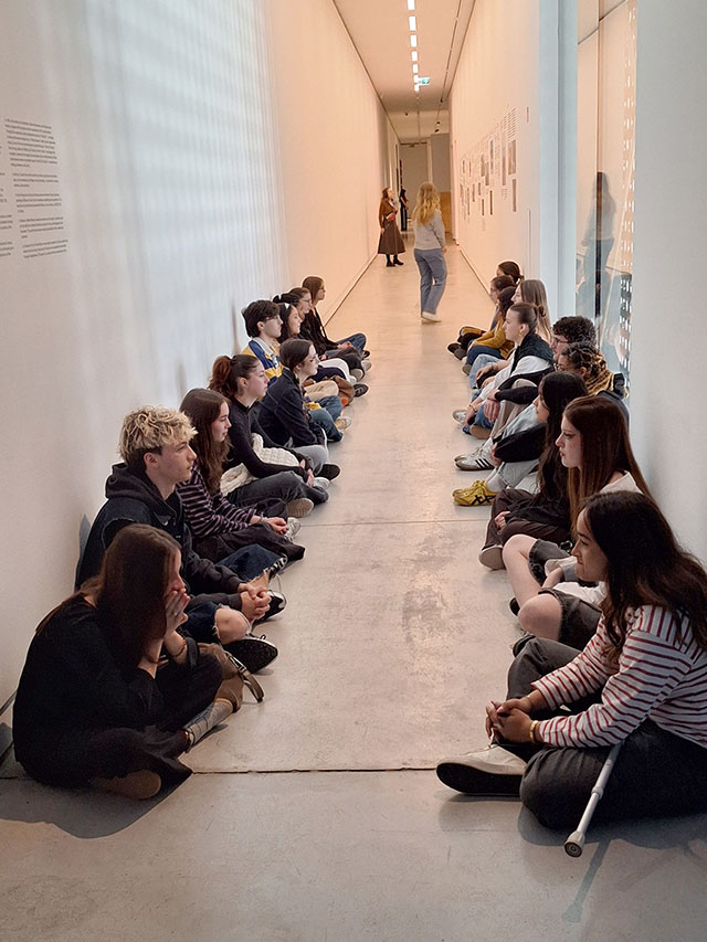 Dijaki sedijo v dveh dolgih vrstah na tleh ozkega, belega osvetljenega galerijskega hodnika. Obrnjeni so drug proti drugemu in izvajajo vajo v pozornosti. Njihova naloga je bila, da nekaj minut v tišini nepremično strmijo drug v drugega. Na stenah so vidni umetniški napisi in dokumentacija.