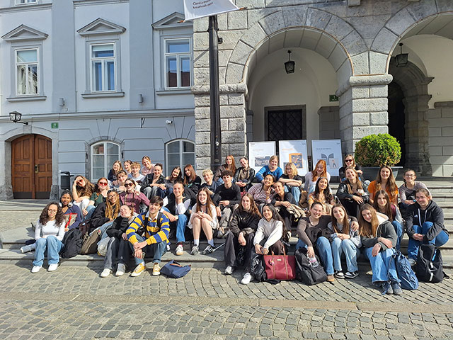 Dijaki so zbrani na stopnicah pred ljubljansko Mestno hišo. Sedijo in stojijo v več vrstah. So nasmejani.