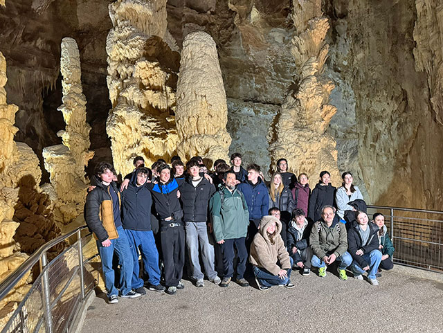 Večja skupina slovenskih in italijanskih dijakov pozira v kraški jami. V ozadju so ogromni kapniki.