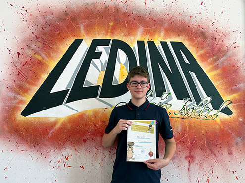 Dijak, prejemnik zlatega priznanja na tekmovanju Bober, v temni polo majici stoji pred steno z velikim grafitom "LEDINA". V rokah drži priznanje.