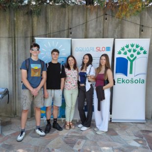 Skupinska fotografija dijakov Gimnazije Ledina z mentorico na zaključni prireditvi projekta Krožnost je naša priložnost. V vrsti stojijo pred panojem z znakom Ekošole.
