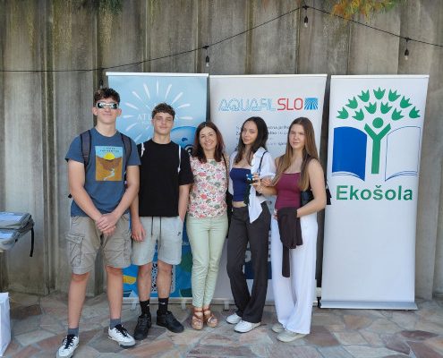 Skupinska fotografija dijakov Gimnazije Ledina z mentorico na zaključni prireditvi projekta Krožnost je naša priložnost. V vrsti stojijo pred panojem z znakom Ekošole.