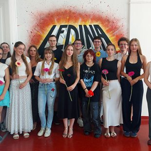 Skupinska fotografija zlatih maturantov pred grafiti steno z napisom Ledina. Štirinajst nasmejanih mladih, nekateri s cvetjem v rokah, pozira v dveh vrstah. Dijaki so oblečeni v raznolika, sproščena poletna oblačila.