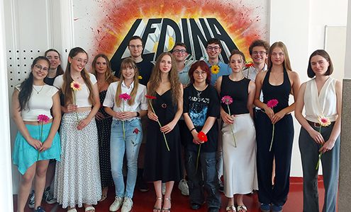 Skupinska fotografija zlatih maturantov pred grafiti steno z napisom Ledina. Štirinajst nasmejanih mladih, nekateri s cvetjem v rokah, pozira v dveh vrstah. Dijaki so oblečeni v raznolika, sproščena poletna oblačila.