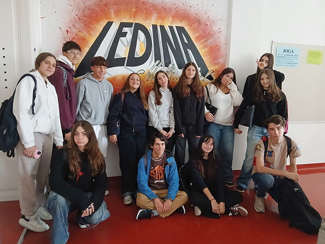 Skupinski posnetek dijakov na hodniku šole pred steno z velikim grafitom z napisom "LEDINA".
