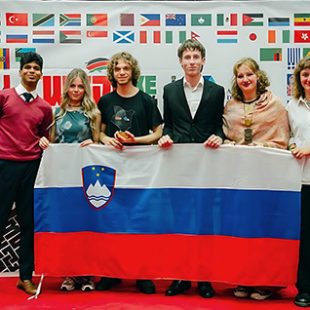 Skupina petih slovenskih debatnic in debatnikov, ki na odru pred steno z zastavami držav udeleženk držijo razprostrto slovensko zastavo. Levo poleg njih stoji predstavnik organizatorjev.