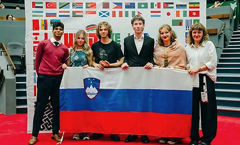 Skupina petih slovenskih debatnic in debatnikov, ki na odru pred steno z zastavami držav udeleženk držijo razprostrto slovensko zastavo. Levo poleg njih stoji predstavnik organizatorjev.