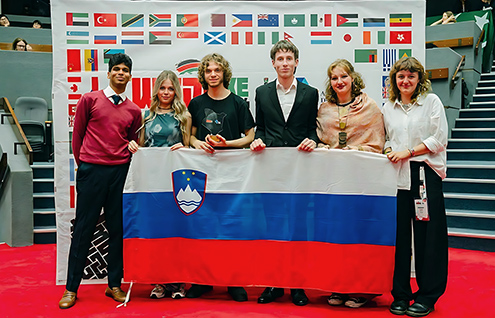 Skupina petih slovenskih debatnic in debatnikov, ki na odru pred steno z zastavami držav udeleženk držijo razprostrto slovensko zastavo. Levo poleg njih stoji predstavnik organizatorjev.