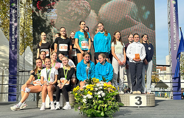 Na zmagovalnem odru stojijo tri skupine tekmovalk iz treh različnih šol. Nekatere držijo v rokah priznanja, nekatere imajo okrog vratu medaljo.