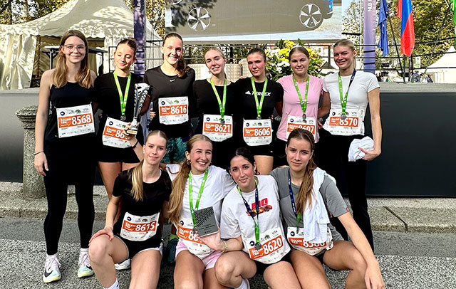 Tekačice z medaljami okrog vratu. Spredaj štiri čepijo, za njimi jih šest stoji. So nasmejane.